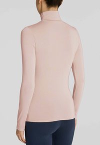Maglietta a maniche lunghe di un delicato rosa chiaro con colletto alto, realizzata in un morbido tessuto testurizzato, dal design attillato con spacchi laterali, abbinata a leggings scuri.