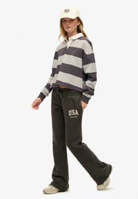 Grå og marineblå stribet cropped sweatshirt med hvid krave, parret med mørke sweatpants med "USA"-tekst. Beige kasket og lyse sko.