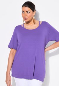 Lila t-shirt med kort ärm och rundad hals, med lager av band vid axlarna och en avslappnad passform. Slät textur och sidslitsar.