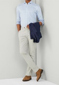 Chemise à rayures bleu clair à boutons, pantalon gris pâle, chaussures en daim marron, et une veste bleu marine portée sur le bras. Coupe moderne avec un design ajusté.
