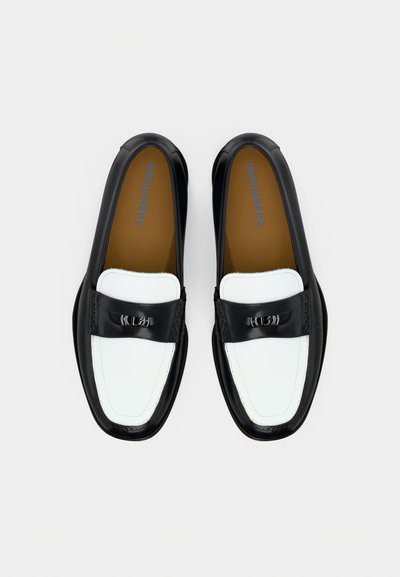 Μοκασίνια σε ασπρόμαυρο με λείο δερμάτινο επάνω μέρος, διακοσμημένα με λευκή μύτη, διακοσμητικά εξαρτήματα και επένδυση με μαξιλαράκι για άνεση.