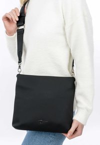 Svart crossbody-väska i slätt material, med en stilren rektangulär form, justerbar rem och subtil logodetalj på framsidan.