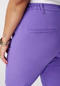 Paarse, rekbare broek met een soepele textuur, elastische tailleband en een subtiele achterzakdetail. Minimalistisch ontwerp zonder patronen.