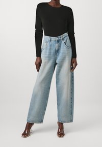 Schwarzer Langarm-Body kombiniert mit hochgeschnittenen, hellblauen weit geschnittenen Jeans; glatte Textur und klassisches Fünf-Taschen-Design.