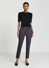 Haut en tricot noir à manches courtes, associé à un pantalon tailleur gris foncé et des escarpins noirs à bout pointu ornés d'une ceinture en or.