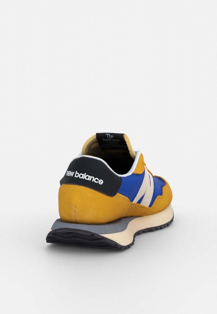 Geel en blauwe sneaker met een bovenwerk van suede en mesh, witte accenten, gewatteerde kraag en rubberen zool, voorzien van het "new balance" logo.