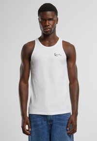 Hvitt tank topp laget av ribbet stoff, med rund hals og en liten svart logo på venstre bryst. Brukt med blå jeans.