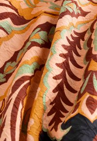 Tissu avec des motifs ondulés répétés en marron, orange, vert et rose, montrant la texture et les plis.