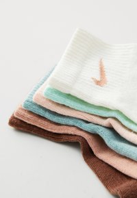 Montón de calcetines coloridos en tonos pastel, que incluyen blanco, verde menta, rosa claro, marrón y aqua, con un logo visible en el calcetín blanco.