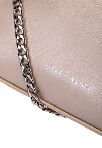 Borsa a mano in pelle beige con superficie texturizzata, dotata di una tracolla in catena argentata e del logo "GERRY WEBER" in bianco. 