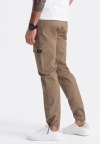 Khaki cargo kalhoty s tapered střihem, stahovací šňůrkou na kotnících, více kapsami a prošívanými detaily, doplněné o bílé tenisky.
