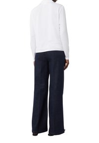 Camicia polo bianca a maniche lunghe con colletto abbinata a pantaloni ampi blu scuro. Il tessuto sembra morbido e liscio.
