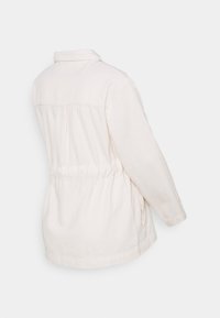 Ljus beige jacka med krage, elastisk midja och två sidofickor. Tillverkad av mjukt tyg med en något strukturerad yta.