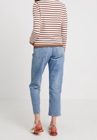 Langes gestreiftes Hemd in Creme- und Brauntönen, kombiniert mit hellblauen Jeans mit geradem Bein und lässigen weißen Turnschuhen mit orangefarbenen Akzenten.