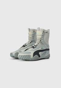 Kotníkové boty ve světle šedé a černé barvě. Mají texturované materiály, gumové podrážky s hroty a elastické lemy pro pohodlné přilnutí.