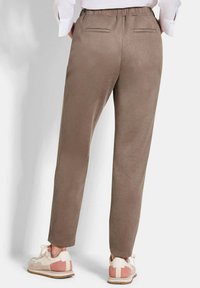 Bruine, zachte stoffen broek met een taps toelopend ontwerp, elastische tailleband en twee achterzakken. Gepaard met lichtgekleurde sneakers.
