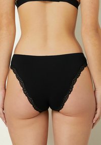 Perizoma di cotone nero con bordi in pizzo, caratterizzato da una texture liscia e un design semplice ma resistente.