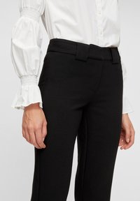 Svarta skräddarsydda byxor med en mjuk textur, med en bred midja och smal passform. Kombineras med en vit blus med puffärmar.