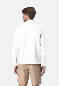 Camicia bianca a maniche lunghe con colletto e polsini abbottonati, abbinata a pantaloni corti beige. Tessuto liscio con una vestibilità comoda e senza motivi visibili.