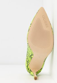 Escarpin à talon haut à motif peau de serpent vert et noir, avec un bout pointu, une texture lisse, et une semelle nue présentant des détails rainurés et une marque.