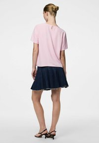 Top corto a maniche corte di colore rosa con texture e schiena a chiave, abbinato a una gonnellina di jeans scuri a campana con bordi sfrangiati. Sandali neri con cinturini.
