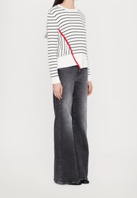 Pull rayé blanc et marine avec un accent rouge, associé à un jean en denim gris taille haute et large. Texture lisse et coupe décontractée.