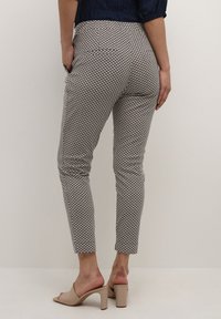 Mönstrade byxor i beige, navy och vitt. Har små geometriska mönster och bakfickor. Bärs med ljusa klacksandaler.