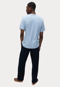 Camiseta de algodón azul claro con cuello redondo, combinada con pantalones de pijama oscuros, suaves y holgados, usados descalzo.