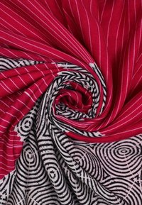 Tessuto a motivo rosso e nero, con strisce bianche su sfondo rosso e disegni circolari neri su sfondo bianco, texture morbida, drappeggiato a spirale.