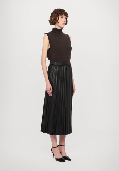 Maglione smanicato a collo alto marrone scuro abbinato a una gonna midi plissettata in pelle nera e tacchi a punta neri.