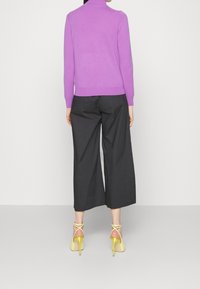 Lilla strikket sweater med høj hals, parret med sorte bredde ben bukser og gule højhælede sandaler. Enkel og moderne silhuet.