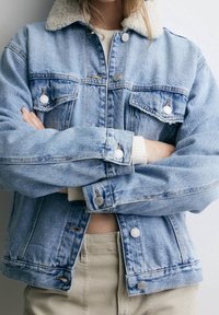 Vaaleansininen farkkutakki, jossa on shearling-kaulus, nappikiinnitys ja kaksi rintataskua. Ominaisuuksiin kuuluu rento malli ja hieman kuluneet yksityiskohdat.