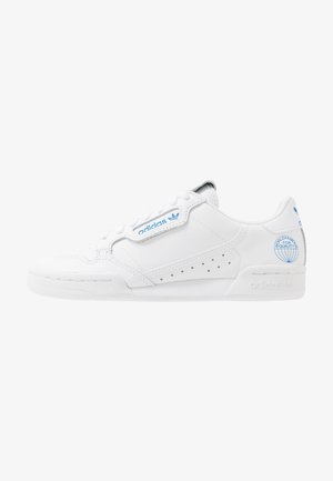 Baskets basses Adidas blanches avec marquage bleu, panneau latéral perforé et logo « World Famous for Quality » près du talon sur fond blanc.