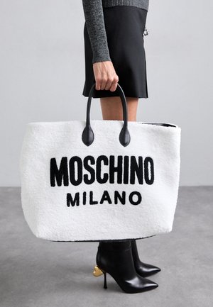 Hvid plyspose med sort "MOSCHINO MILANO" tekst, der har sorte læderhåndtag. Blevet ledsaget af sorte hæle støvler med guld accenter.