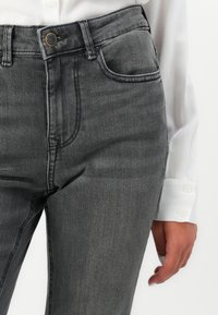 Jeans gri din denim, cu un design ajustat, stil cu cinci buzunare și efecte subtile de uzură. Construit dintr-un material texturat.