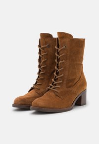 Bottines en daim marron avec un design à lacets, dotées d'un petit talon bloc et d'une texture lisse. Des coutures latérales ajoutent du détail.