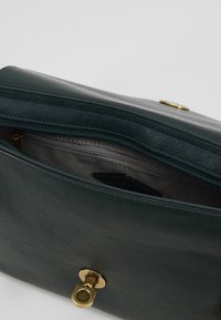 Borsa verde in pelle con apertura con zip, hardware dorato e interno testurizzato. Il design esterno presenta una superficie liscia e una chiusura magnetica.
