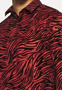 Camicetta a righe zebrate rossa e nera realizzata in tessuto testurizzato, con colletto a bottone e design aderente.