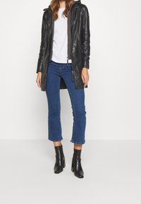 Schwarze Lederjacke mit Kapuze, graue Innenschicht, weißes T-Shirt, blaue cropped Jeans und schwarze stiefeletten mit Absatz.