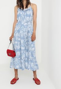 Jasnoniebieska midi sukienka w kwiaty z falbaniastym dekoltem, wcięciem w talii i warstwowym dołem. W połączeniu z czerwoną torebką i czerwonymi sandałami w paski.