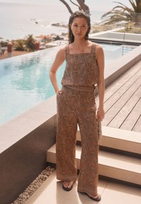 Kaheosaline komplekt, mis sisaldab pruuni crop top'i ja laia jala pükse, millel on ringikujulised ja lineaarsed mustrid, valmistatud kergest materjalist.