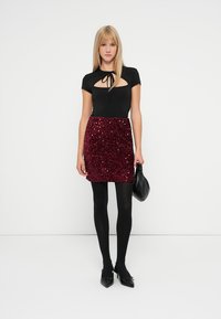 Body negru, ajustat, cu o decupare în formă de cheie, asortat cu o fustă mini bordeaux cu paiete. Colanți negri și o geantă mică neagră completează ținuta.