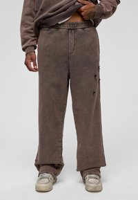 Bruine oversized broek met een gestructureerde afwerking, voorzien van rafelige randen en kleine scheuren. Elastische tailleband voor comfort. Gecombineerd met sneakers.