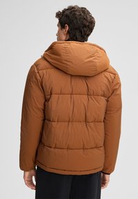 Giacca imbottita marrone con cappuccio, dotata di una fantasia trapuntata e polsini elasticizzati. Forma del corpo semplice con una texture liscia e opaca.