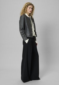 Szürke bőrdzseki croppolt dizájnnal, gombos záródással és kerek dekoltázzsal. Magas derékú, fekete, széles szárú nadrággal párosítva.