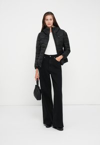 Black quilted puffer jacket with a high collar, worn over a white top, paired with high-waisted black wide-leg jeans and a black bag.