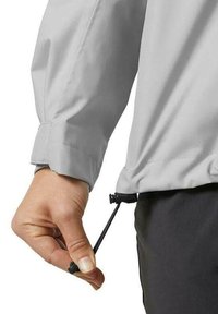 Light gray waterproof jacket with elastic cuffs and a drawstring bottom being adjusted by a hand. The fabric appears smooth and durable.