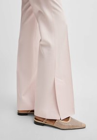 Jasnoróżowe spodnie szerokie z bocznymi rozcięciami, połączone z beżowymi balerinkami z wzorzystą tekstylną górą i cienkimi paskami na kostce.