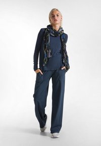 Maglia a maniche lunghe blu navy con vestibilità morbida, abbinata a pantaloni larghi scuri con tasche laterali e una sciarpa multicolore a fantasia.