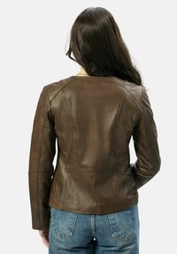 Bruine leren jas met een getailleerd ontwerp, voorzien van gestikte details en lange mouwen, gecombineerd met blauwe high-waisted jeans.